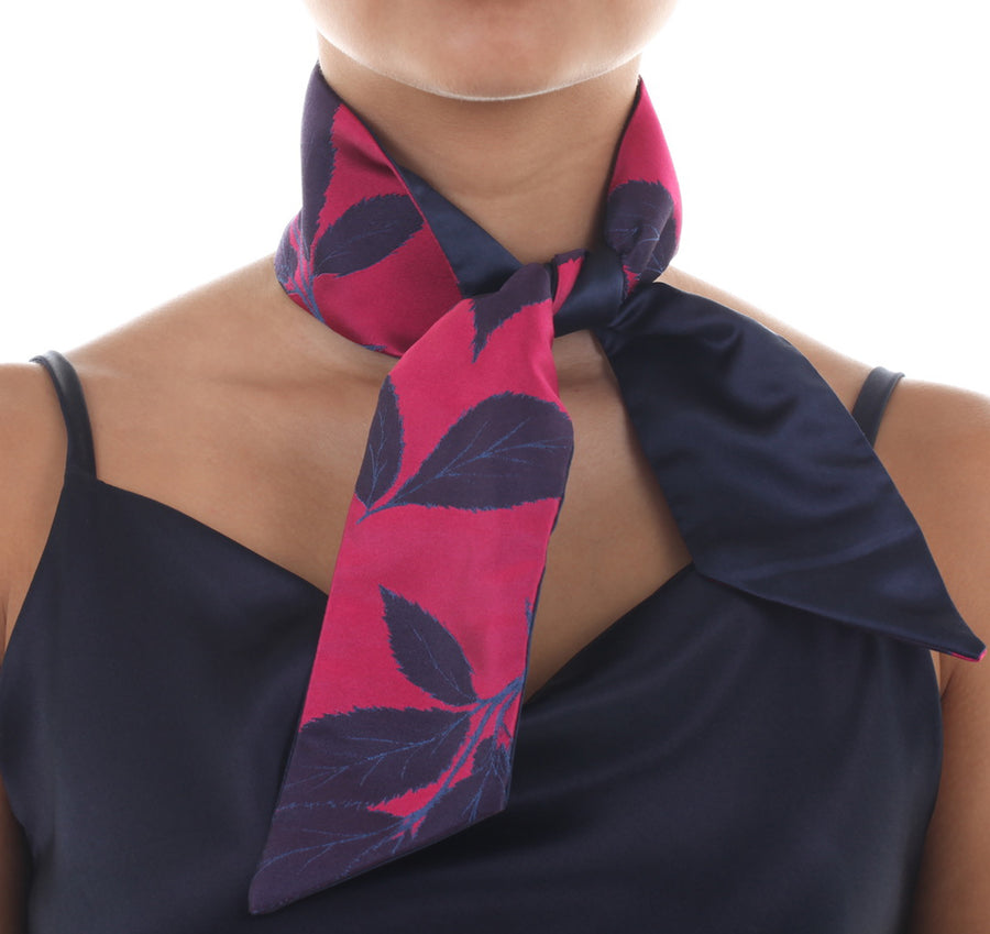 Female model in magenta silk Mimi Fong skinny scarf with blue leaves pattern, tied elegantly around neck on a white background