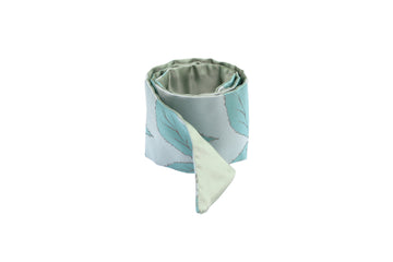 Rolled light green silk Mimi Fong skinny scarf with leaves pattern on white background