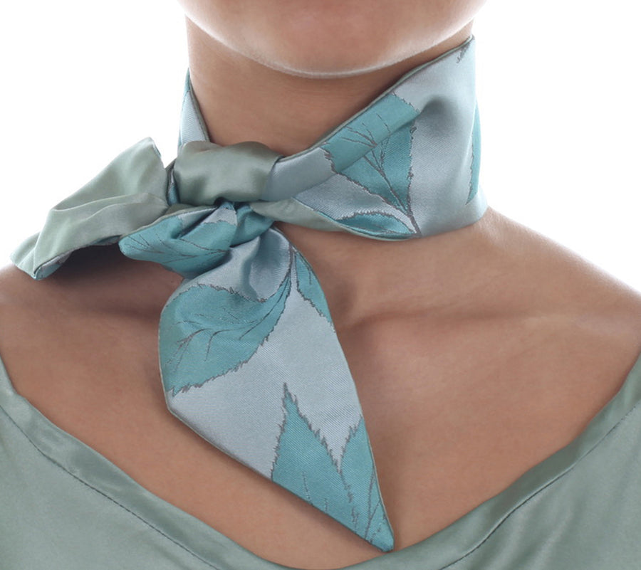 Female model in light green silk Mimi Fong skinny scarf with leaves pattern, tied elegantly around neck on a white background